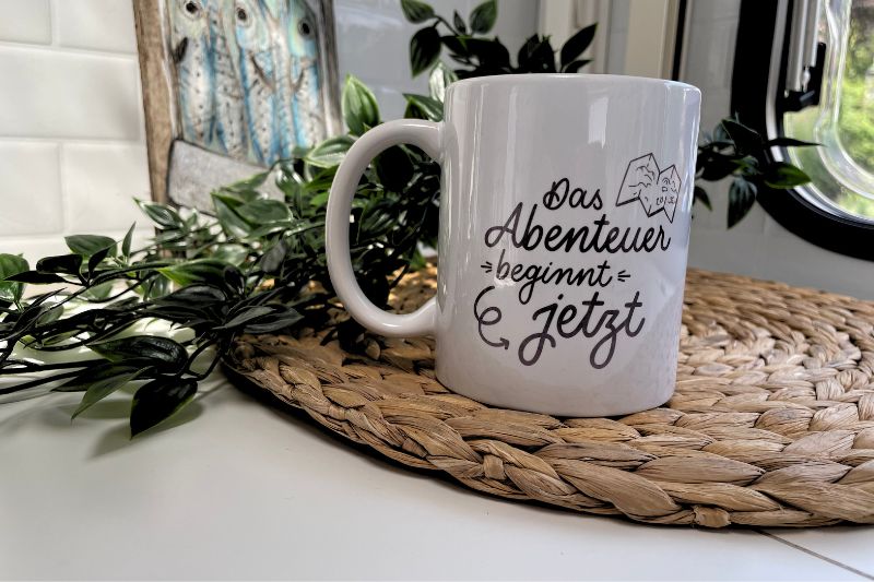 Tasse sublimiert mit Design des Monats "Das Abenteuer beginnt jetzt"