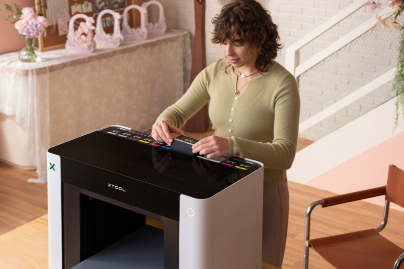xtool-omni-dual-uv Eine Frau steht hinter dem xTool O1 Omni Printer und wechselt die Farbkartuschen