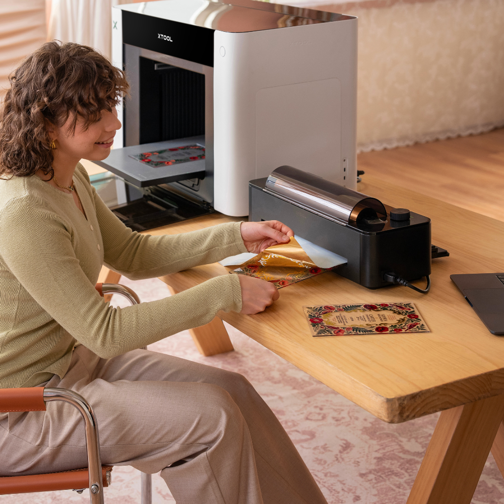 Eine Frau betätigt das Laminiergerät für den xTool O1 Omni Printer und nutzt eine Goldfolie