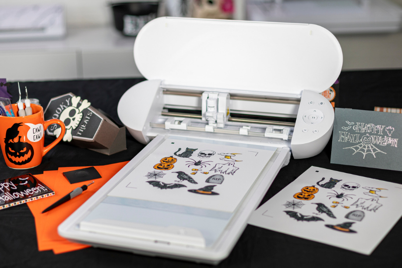 Das Bild zeigt einen Plotter, in den ein bedruckter Stickerbogen mit Halloween-Motiven eingelegt ist.