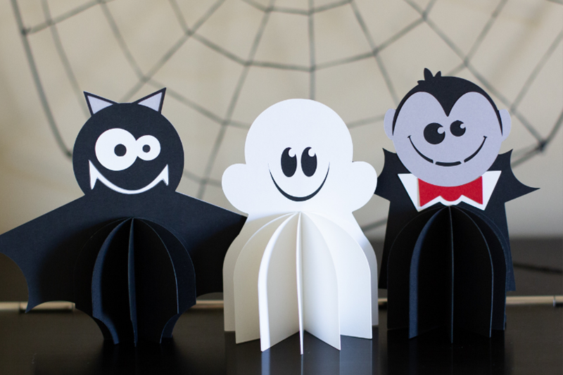 Das Bild zeigt Halloween Tischdeko aus Pappe in Form einer Fledermaus, eines Geistes und eines Vampiers.
